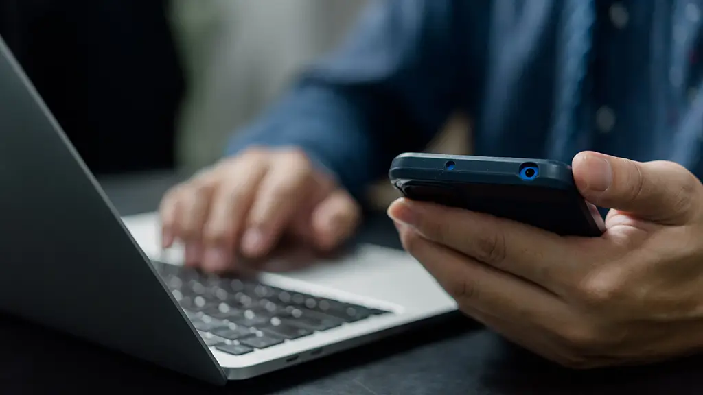 Mann bedient Laptop und Smartphone